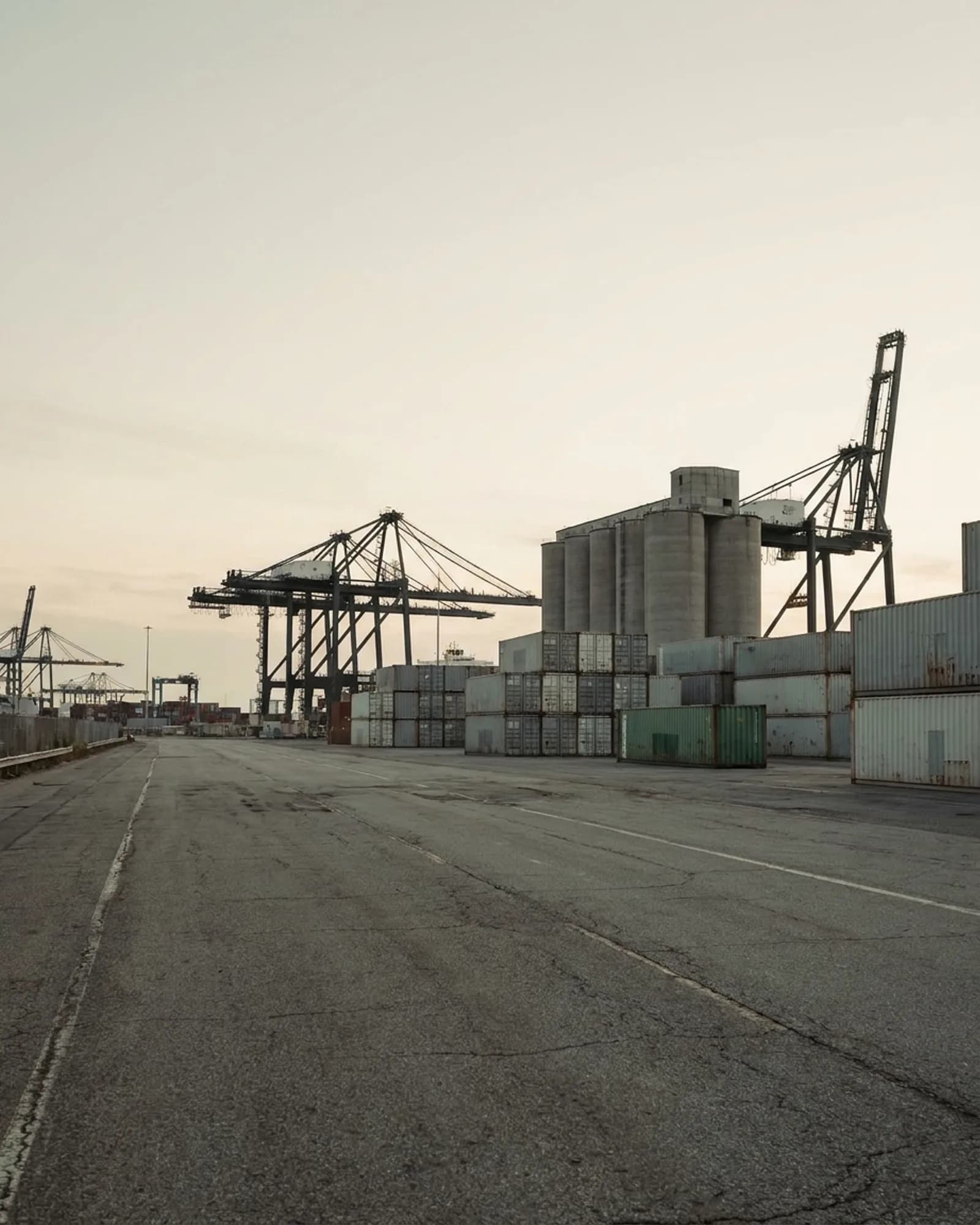 Terminal industrial ao fim do dia, com pilhas de contêineres, pórticos e silos ao fundo